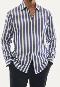 Camicia a righe blu e bianche in tessuto leggero, con chiusura frontale a bottoni, maniche lunghe e orlo curvo.