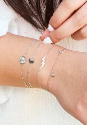 Vier zilveren kettingarmbanden om een pols. De ontwerpen omvatten een zonnestraal, halve manen, een zigzag bliksemschicht en een ster charm.
