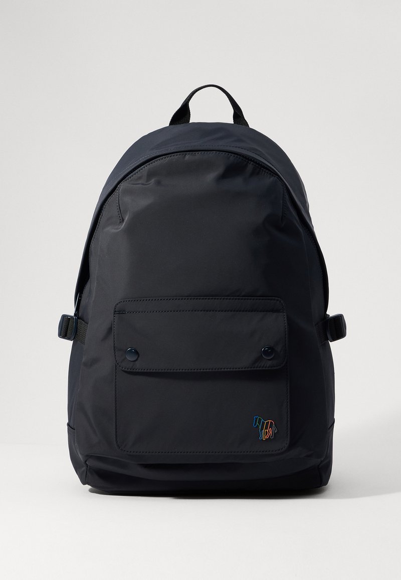 Mørkeblå nylon ryggsekk med rund form, frontlommepose, to trykknapper og en fargerik broderidetalj nederst.