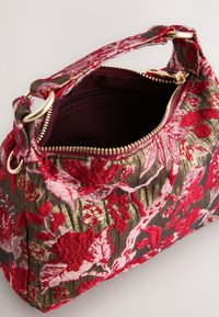 Kleine Handtasche mit roter und pinker Blumenstickerei, goldenem Reißverschluss und passendem Stoffgriff mit goldenen Ringen auf hellem Hintergrund.