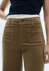 Bruine corduroy broek met een hoge taille, voorzien van voor- en achterzakken en een knoopsluiting, met een ribbeltextuur.