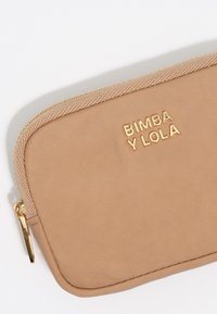 Bolsa de tela beige con el logotipo dorado "BIMBA Y LOLA". Presenta un cierre texturizado y una superficie lisa y sin adornos.