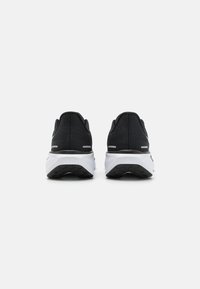 Sapatos atléticos pretos com um superior texturizado, salto redondo, entressola branca e sola de borracha preta. Apresentam acentos minimalistas.