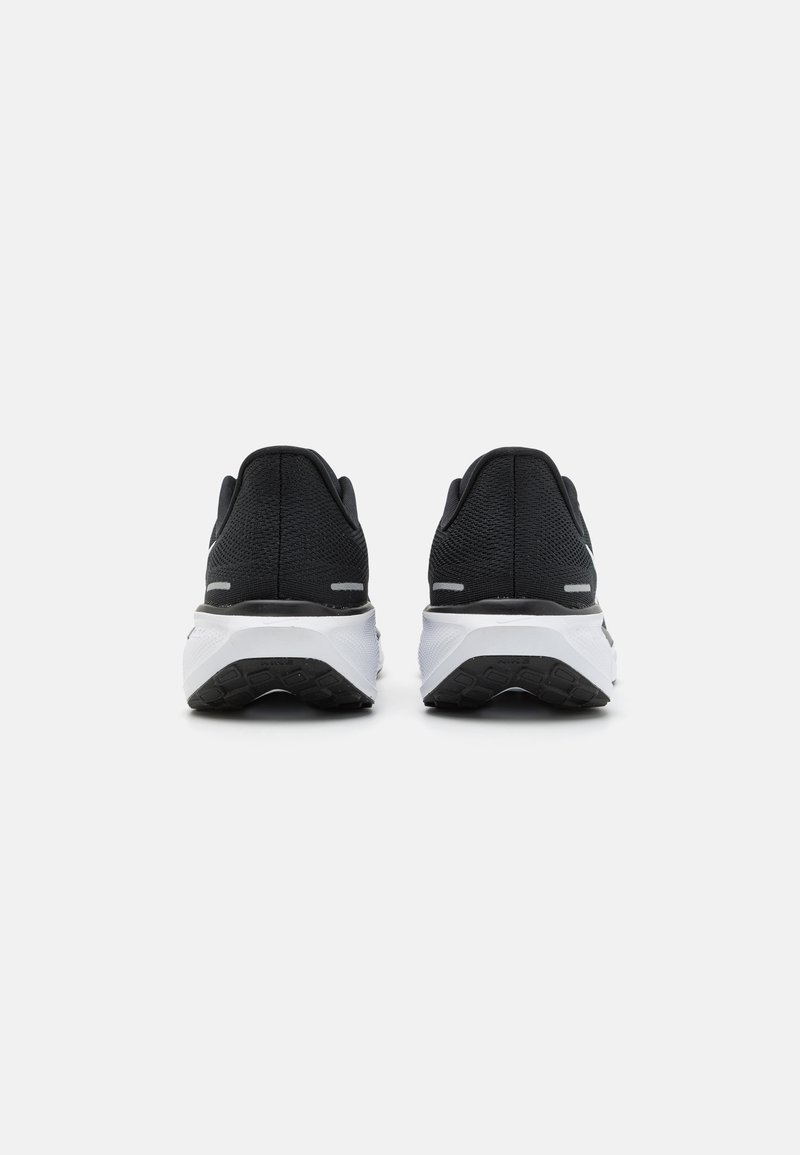 Zapatos deportivos negros con parte superior texturizada, tacón redondo, entresuela blanca y suela exterior de goma negra. Presentan acentos minimalistas.