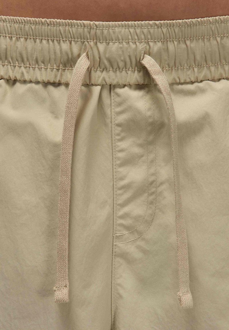 Shorts beiges avec une taille élastique, dotés d'un cordon de serrage et de détails sur les coutures latérales. Texture lisse et tissu léger.