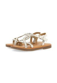 Witte sandaal met sprankelende decoratieve versieringen, meerdere gekruiste banden en een verstelbare enkelgesp. Platte zool met een lichtbruine basis.