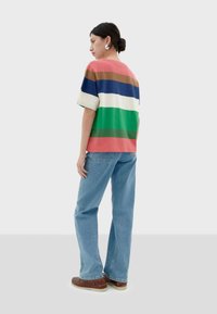 Striped short-sleeve knit top featuring colors: pink, cream, blue, green, and brown, paired with light blue jeans and brown shoes.