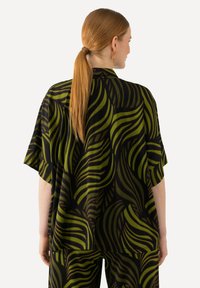 Short-sleeve shirt in black fabric featuring a green and dark brown leaf pattern. Relaxed fit with a straight hem and soft texture.