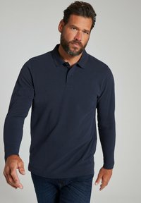 Navyblaues langärmliges Poloshirt mit kragenlosen Ausschnitt, zwei-Doppelkknopf-Leiste und glattem Material, kombiniert mit dunklen blauen Jeans.