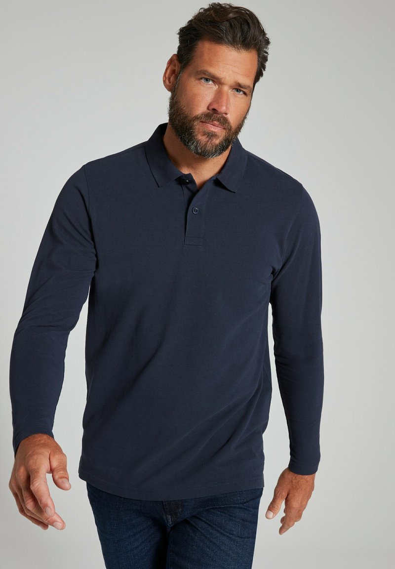 Navyblaues langärmliges Poloshirt mit kragenlosen Ausschnitt, zwei-Doppelkknopf-Leiste und glattem Material, kombiniert mit dunklen blauen Jeans.