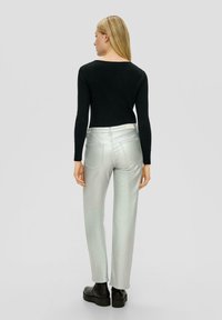 Zwarte geribbelde longsleeve top gecombineerd met metallic zilveren rechte broek en chunky zwarte enkellaarzen, gezien vanuit de achterkant.