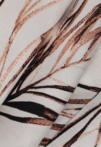 A világos bézs alapú textil, absztrakt barna és fekete levélmintákkal. Az anyag puha és texturált megjelenésű, mélységet teremt.