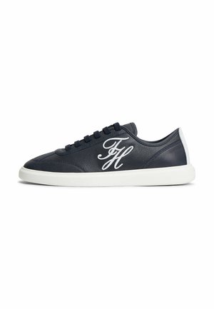 Czarne skórzane niskie sneakersy z białym logo w stylu pisma po boku oraz białą podeszwą i pętelką na pięcie, widoczne z zewnętrznej strony.