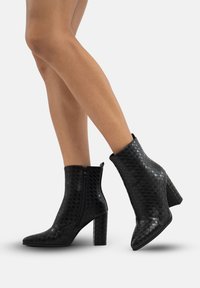 Botines negros hasta el tobillo con textura trenzada, punta afilada y tacón grueso. Presentan un cierre lateral y un acabado suave.