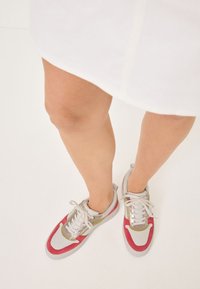 Sneakers featuring a design with a white upper, gray soles, red accents, and metallic details; lace-up with a smooth texture.