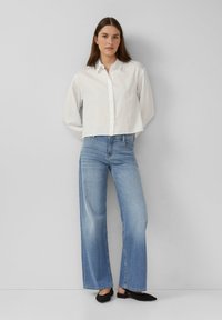 Camisa blanca de botones, recortada y de corte relajado; jeans de pierna ancha de color azul claro; zapatos negros de slip-on; tejido suave con un aspecto informal.