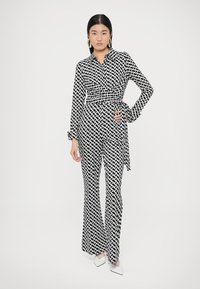 Zwart-wit jumpsuit met patroon, voorzien van een kraag, lange mouwen en een getailleerde taille met een strik. Uitlopende pijpen en een gladde stof.