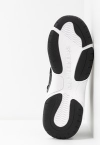 Černobílá podrážka tenisky s texturovanou gumou pro lepivost, hladkým bílým mezipodešví a vyraženým logem "Calvin Klein Jeans".