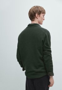 Tmavě zelené polo tričko s dlouhým rukávem, měkkou texturou a límečkem, s vyhrnutými rukávy a volným střihem, pohled zezadu.