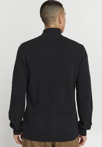 Marineblå strikket sweater med høj krave, tekstureret strikmønster på skuldrene og ribbede manchetter og kant, som giver et struktureret udseende.