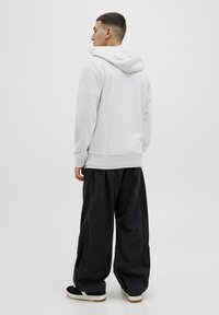Sudadera gris con capucha y corte relajado, que presenta un dobladillo y puños acanalados, combinada con pantalones negros holgados y zapatillas negras.