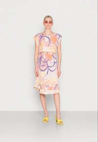 Vestido flores coloridas com um corte descontraído, mangas curtas e bainha com franzido. Combinado com sandálias amarelas e óculos de sol cor-de-rosa.