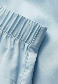 Tissu bleu clair avec couture visible et détail d'une ceinture élastique.