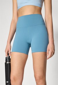 Shorts atletici de culoare albastră, confecționați dintr-un material elastic, cu o talie înaltă. Designul prezintă o textură netedă și detalii decorative de cusătură curate.