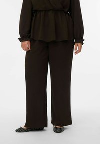 Haut à manches longues brun foncé texturé avec taille peplum, associé à un pantalon large brun foncé et des ballerines noires à motifs.