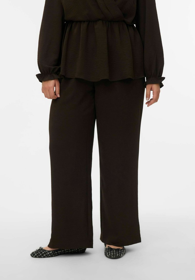 Haut à manches longues brun foncé texturé avec taille peplum, associé à un pantalon large brun foncé et des ballerines noires à motifs.