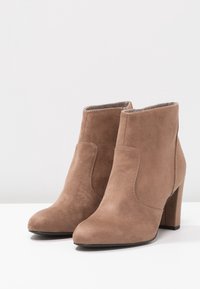 Kulaté hnědé kotníkové boty z broušené kůže s hladkou texturou. Mají potažený blokový podpatek a minimální dekorativní švy.