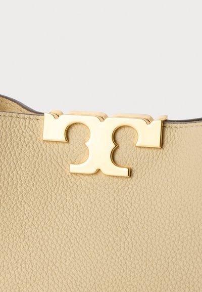 Beige Lederhandtasche mit strukturierter Oberfläche und einem goldfarbenen Verschlussakzent mit einem stilisierten Initialdesign.
