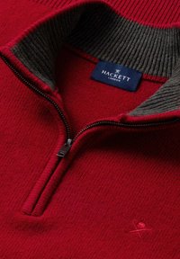 Roter Reißverschluss-Pullover mit einem gerippten grauen Kragen, ausgestattet mit einem Metallreißverschluss und dezentem Logo-Stickerei auf der Brust. Strukturierter Strickstoff.