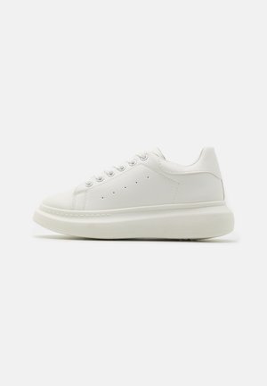 Hvit lær sneakers med rund tå, flat gummisa sole, seks hull for snøring og perforerte detaljer på siden for ventilasjon.