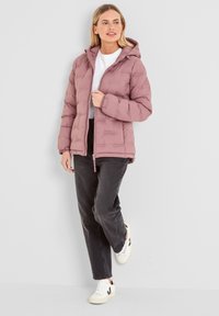 Padded pink jacket with a hood, zip closure, and elastic cuffs. Worn with a white shirt, black pants, and white sneakers.