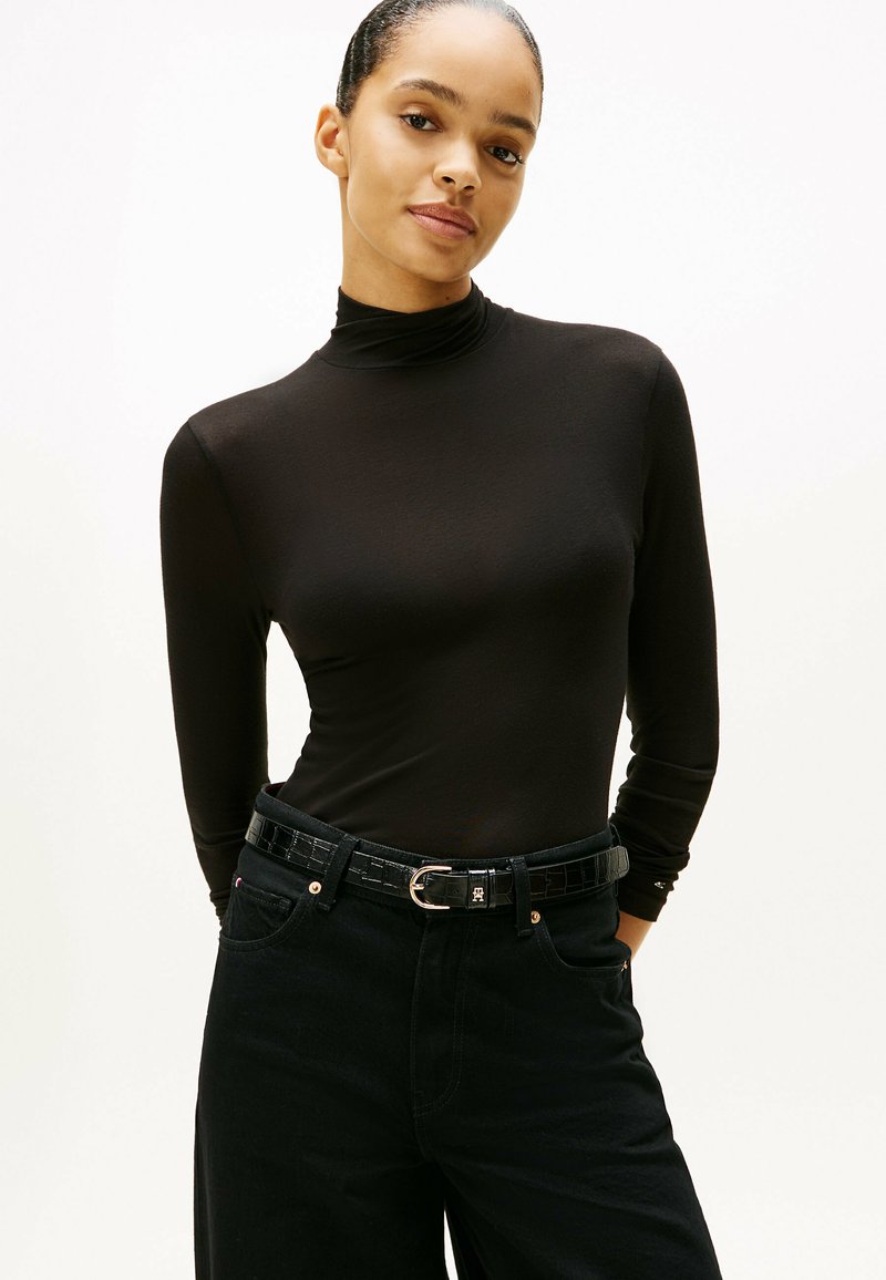 Zwarte langemouw turtleneck top gemaakt van een gladde stof, gecombineerd met hoge zwarte broek en een gestructureerde riem met een zilveren gesp.