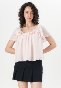 Blusa trasparente rosa chiaro con colletto arricciato e maniche corte, abbinata a una gonna nera a pieghe. Tessuto morbido e fluttuante e vestibilità rilassata.