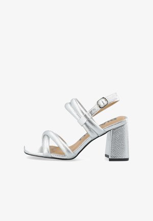Silver heeled sandals with a textured finish, open toe, and three cross straps. Features a metallic block heel and an adjustable ankle strap.