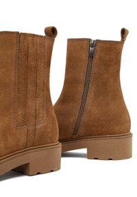 Botas de ante marrón hasta el tobillo con un acabado texturizado, que cuentan con un cierre de cremallera, una lengüeta y una suela de goma gruesa con un patrón estriado.