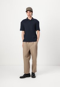 Navy short-sleeve ribbed polo, beige pleated trousers, and black leather shoes. A plaid cap completes the outfit. Simple and modern layout.
