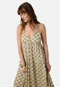 Robe maxi arborant un imprimé palmier dans des tons de vert, de marron et de beige. Fabriquée en tissu léger, avec des bretelles spaghetti ajustables et une silhouette fluide.