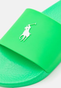 Grön gummisandalslide med en texturerad rem som har en vit polo-spelare-logotyp. Sulan har en slät, profilerad design.