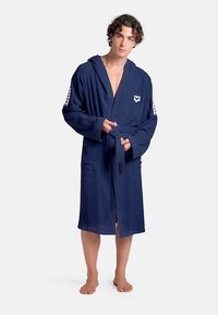 Marineblauwe badjas van zachte, textuurrijke stof met capuchon, voorstrik en zijzakken; heeft een merklogo en contrasterende schouderstrepen.