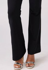Czarne, dopasowane spodnie o gładkiej fakturze i rozszerzanym kroju. Połączone z srebrnymi, paskowanymi sandałami na wysokim obcasie.