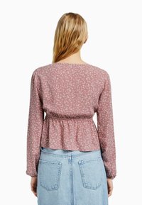 Blusa a fiori rosa chiaro con maniche lunghe, dotata di vita arricciata, vista di spalle con una gonna di jeans blu.