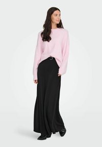 Ροζ πλεκτό πουλόβερ με χαμηλούς ώμους, συνδυασμένο με μια μαύρη φούστα που φτάνει μέχρι το έδαφος. Το σύνολο διαθέτει μαύρη ζώνη και γυαλιστερά μαύρα παπούτσια.