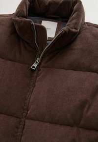 Braune Baumwollcord-Pufferjacke mit hohem Kragen, Reißverschluss und gestepptem Muster, ausgestattet mit einem neutralen Innenfutter und einem Markenlabel.