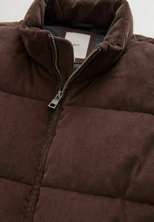 Ruskopolttoisen corduroy-pufferitakki, jossa on korkea kaulus, vetoketjukiinnitys ja tikattu pinta. Takissa on neutraali vuori ja brändilogo.