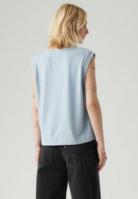 Top di cotone senza maniche di colore azzurro chiaro con vestibilità morbida. La vista dal retro mostra un colletto rotondo e semplici dettagli di cucitura. Abbinato a jeans neri.