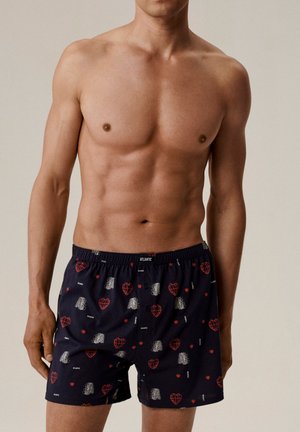 Bokserki w granatowym kolorze z czerwonymi sercami i srebrnymi akcentami. Wykonane z lekkiego materiału, z elastycznym pasem i zapięciem na guzik.
